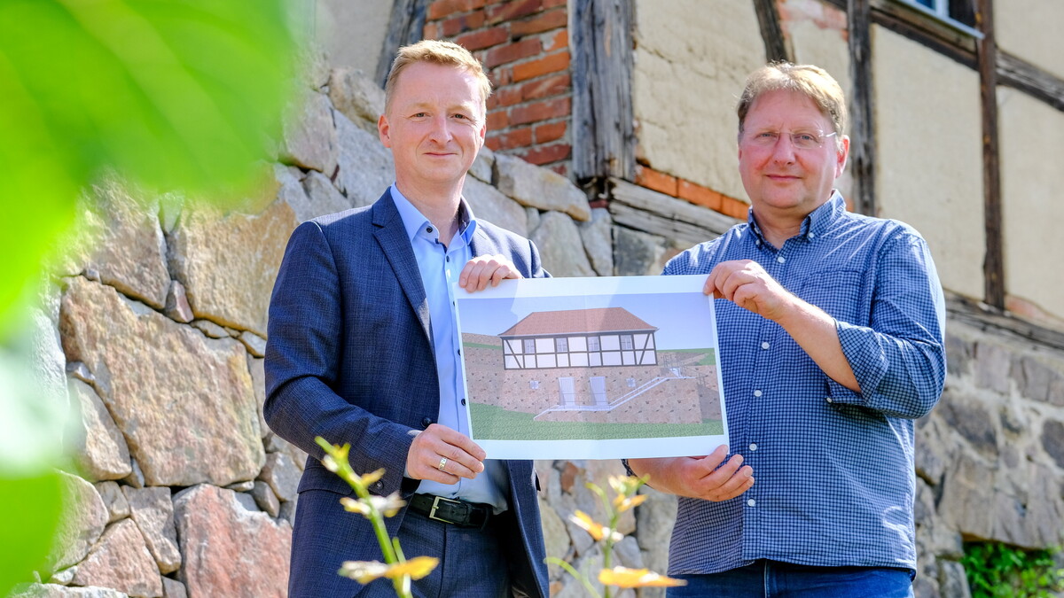 Michael Thomas (l.) und der technische Leiter des Sanierungsprojekts, Lutz Bürger, halten vor dem Winzerhaus eine Zeichnung in der Hand, wie das Gebäude nach Abschluss der Bauarbeiten aussehen wird.