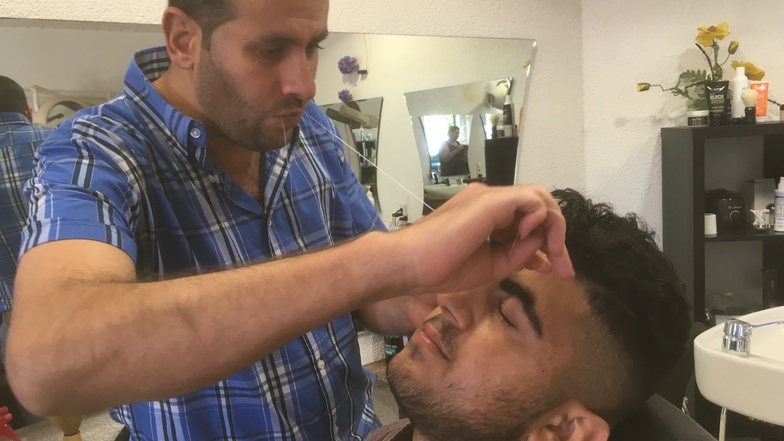 Mit der traditionellen Fadentechnik entfernt der syrische Friseur Waseem störende Haare im Gesicht.