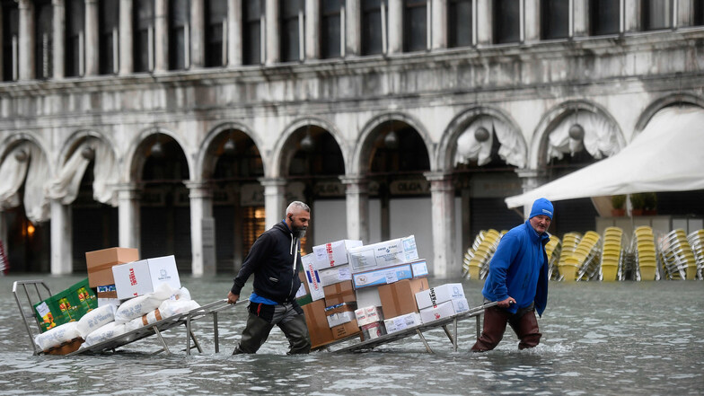 Männer waten mit Kartons und Lebensmitteln, die sie auf einer Trage transportieren, durch das Hochwasser.