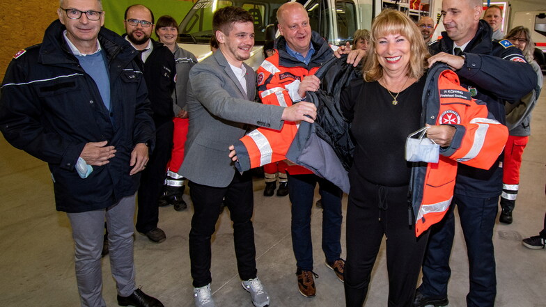 Viele Männerhände helfen Petra Köpping in eine Jacke der Johanniter, die die Leisniger Truppe mit dem Namen der Gesundheitsministerin versehen hat.