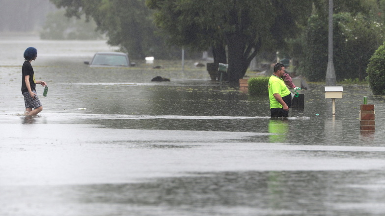 Ein Mann und eine Frau gehen in Windsor über eine überflutete Straße. Tagelanger Starkregen hat im Südosten Australiens zu einem katastrophalen Hochwasser und der Evakuierung ganzer Ortschaften geführt.