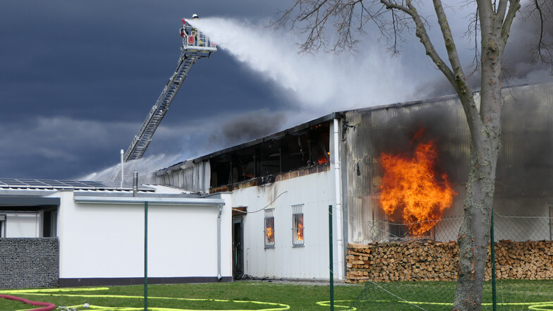 Die Lagerhalle einer Firma in Lüptitz in der Gemeinde Lossatal steht in Brand. Die Feuerwehr geht mit Wasser, unter anderem über eine Drehleiter, gegen die Flammen vor.