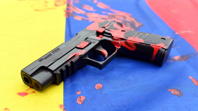 Karlsruhe: Bei einer Protestaktion gegen den Waffenhersteller Sig Sauer liegt auf einer kolumbianischen Fahne eine untauglich gemachte Softairwaffe auf der "·Sig Sauer P226" steht und die mit roter Farbe bekleckert ist.