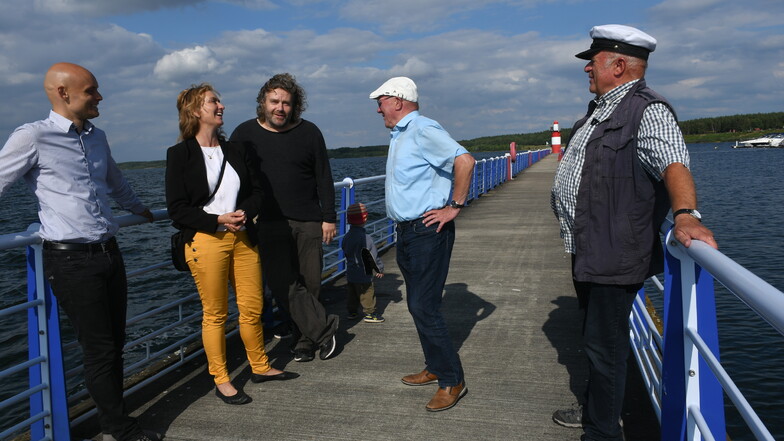 Caren Lay mit den Teilnehmern der Gesprächsrunde auf dem Wellenbrecher im Hafen von Klitten. Im Hintergrund ist der erste Leuchtturm am größten sächsischen Gewässer zu erkennen.