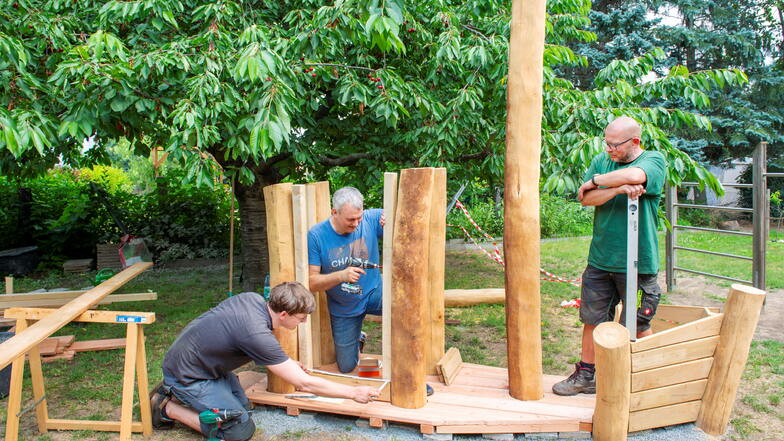 Unter dem aufmerksamen Blick von Lutz Beyer (r.) bauen die Väter Jan Starruß (l.) und Karl Schumacher ein Holzschiff im Garten der Kita „Guter Hirte“ auf.