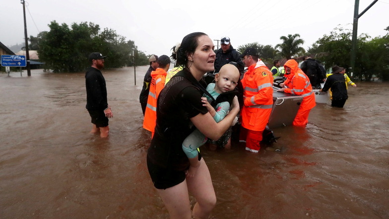 Lismore: Eine Frau trägt ein Baby, während andere Menschen mit kleinen Booten aus dem Hochwasser gefahren werden. Sintflutartiger Regen hat die schweren Überschwemmungen im Osten Australiens weiter verschärft.
