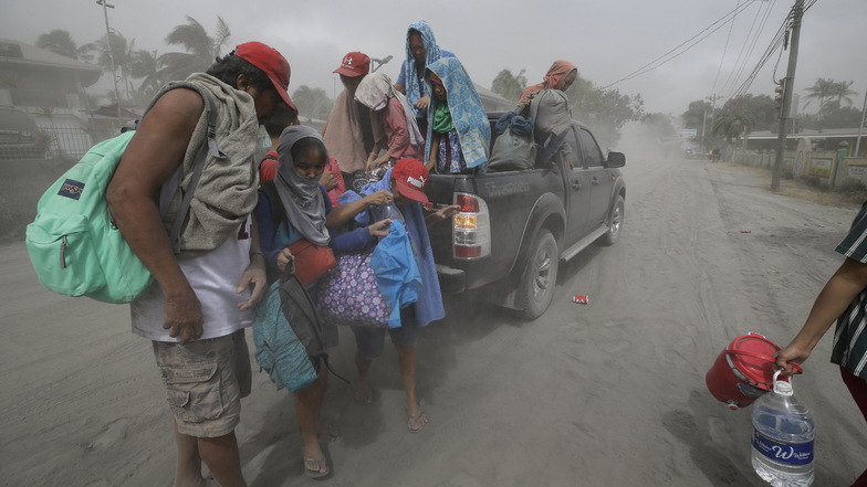 Eine Familie steht auf einer mit Asche bedeckten Straße und bereitet sich während einer Evakuierung auf die Abfahrt aus dem von Vulkan Taal in der südlichen Provinz Cavite bedrohten Gebietes vor.