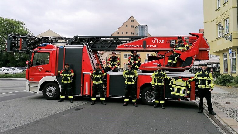 Hauptamtliche der Zittauer und freiwillige Kameraden der Hirschfelder Feuerwehr mit neuer Einsatzkleidung vor der Drehleiter.