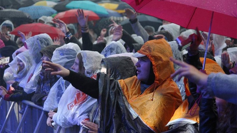 Und so ist der Platz vor der Bühne nicht nur voller Menschen, sondern auch voller Regenschirme.