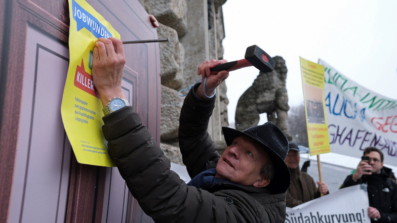 Ein Umweltaktivist nagelt ein Plakat mit den Begriffen „Jobwunder“ und „Killerjob“ an eine symbolische Tür vor dem Neuen Rathaus. Der Protest des Aktionsbündnisses richtet sich gegen den geplanten Ausbau des Frachtflughafens Leipzig/Halle.