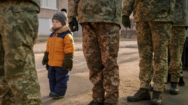 Ein Kind steht neben ukrainischen Soldaten und imitiert ihre Haltung.