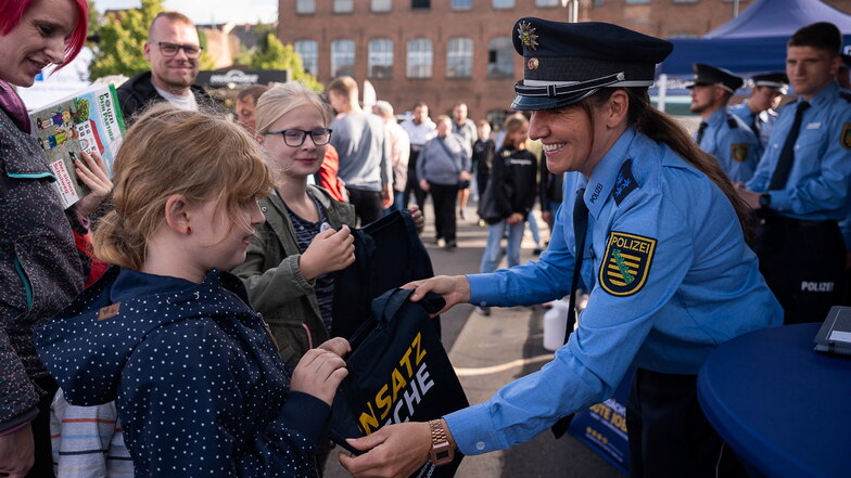 Eine Polizistin überreicht einem Mädchen einen Beutel mit Wissenswertem über die sächsische Polizei.