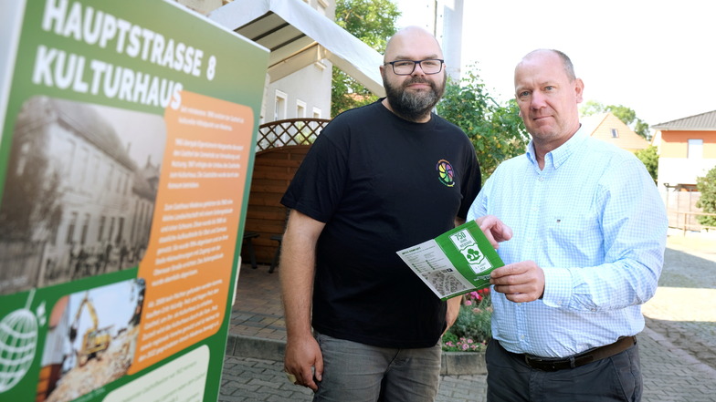 Steffen Uebermuth (v. l.) von Niederau bewegt und Bürgermeister Thomas Claus sind stolz auf die Organisation der 750-Jahr-Feier. Links im Bild ist eine Blechtafel mit geschichtlichen Fakten zum Kulti zu sehen – davon gibt es nun mehr als 50 im Ort.