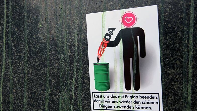 Auch Anti-Pegida-Sticker im Form einer Zigaretten-Werbung kleben am Sockel des Denkmals und zeugen von der Farbattacke.