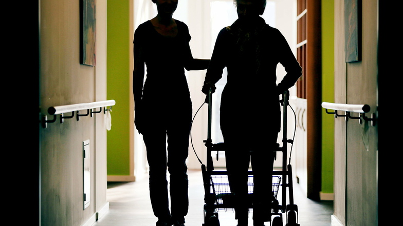 Eine Pflegekraft (l) begleitet die Bewohnerin eines Altenheims mit Rollator. Der Bundestag will 20.000 Hilfspfleger finanzieren.