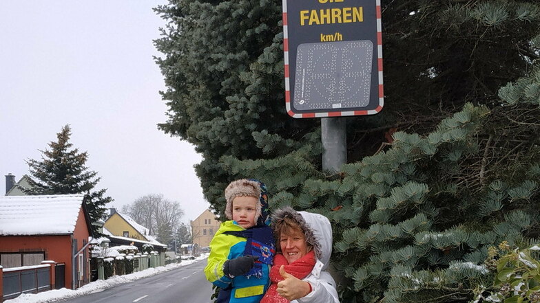 Sylvia Müller aus Oßling freut sich mit ihrem Enkelkind, dass die Geschwindigkeitsanzeigetafel jetzt am Ortseingang steht. Bald kommt noch ein Tempo-30-Schild an die Durchgangsstraße.