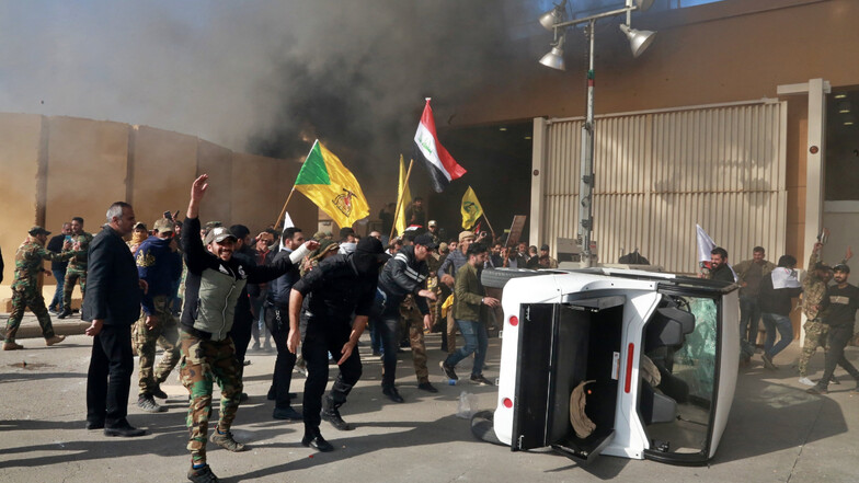 Unterstützer schiitischer Milizen haben vor dem Gebäude der US-Botschaft ein Fahrzeug umgeworfen, während aus dem Gebäude Rauch austritt.