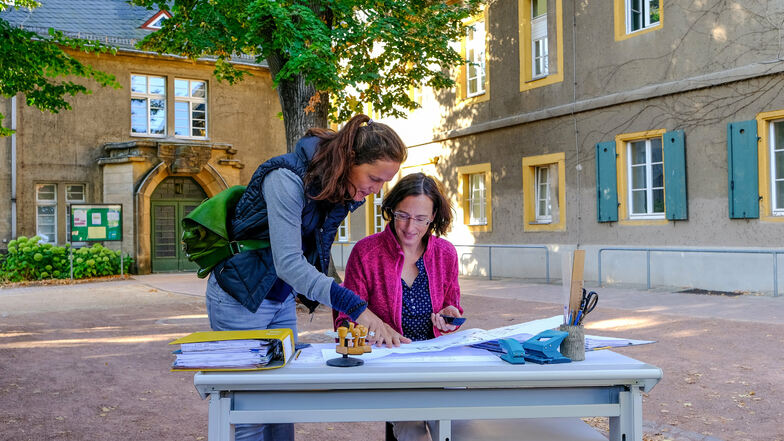 Pfarrerin Annegret Fischer (l.) und Sabine Queißer haben einen Schreibtisch für einen Moment in den Pfarrhof verlegt. Die Aktion symbolisiert, dass die Arbeiten für den Umzug des Pfarramts ins Erdgeschoss begonnen haben.