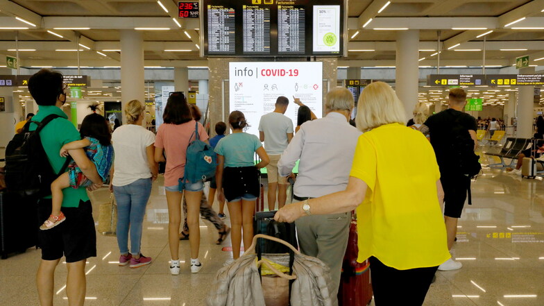 Menschen informieren sich im Abflugbereich des Flughafens von Palma de Mallorca über Corona-Regeln.