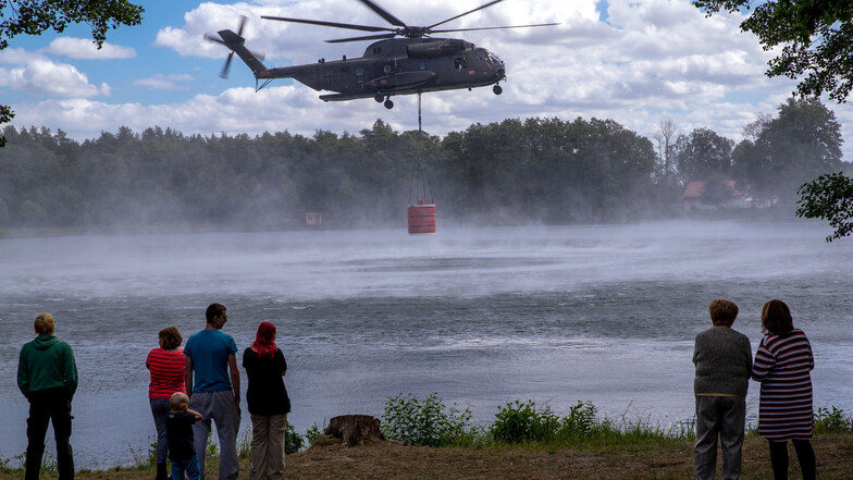 Einwohner und Urlauber beobachten einen Hubschrauber CH53 der Bundeswehr beim Aufnehmen von 5.000 Liter Löschwasser in einem See.