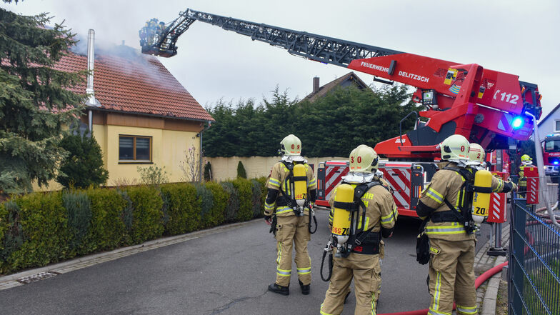 Auf der Drehleiter und unter Atemschutz gehen mehrere Feuerwehrleute gegen einen Dachstuhlbrand in Krostitz vor.
