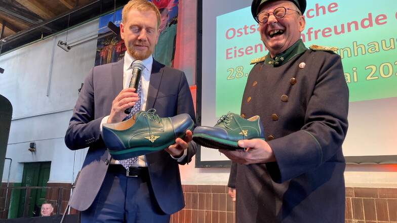Ministerpräsident Michael Kretschmer überreicht Alfred Simm ein Paar maßgefertigter Schuhe, die zu Simms königlich-sächsischer Eisenbahnuniform passen.