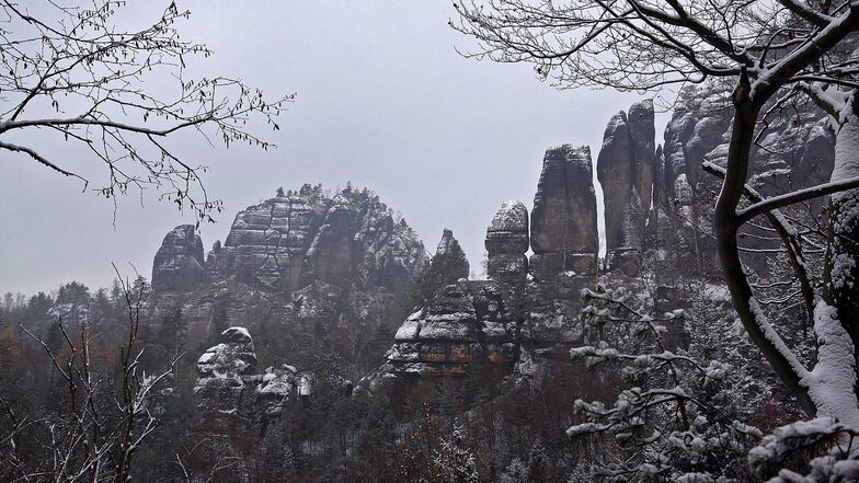 Wie ein gezuckerter Stollen zeigen sich die Felsen im Elbsandsteingebirge im Schnee. Hier der Blick zu den markanten Falknertürmen, im Hintergrund der Rauschenstein.