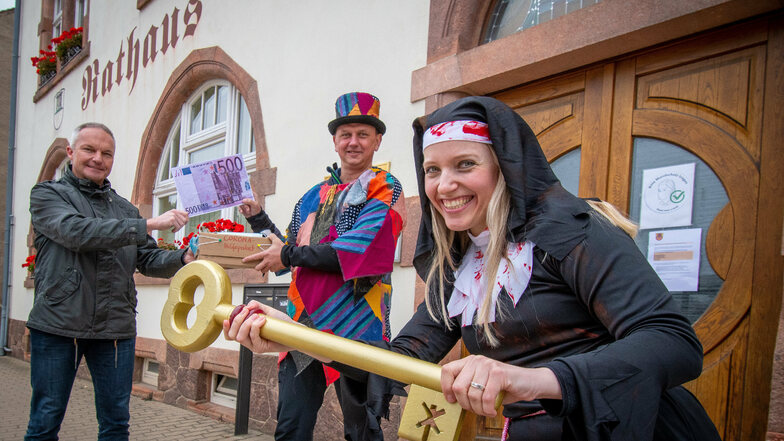 In Ostrau haben Bürgermeister Dirk Schilling (links) und Nonne Denise einen symbolischen Geldschein an Thomas Lohse vom Schrebitzer Carneval-Club überreicht.