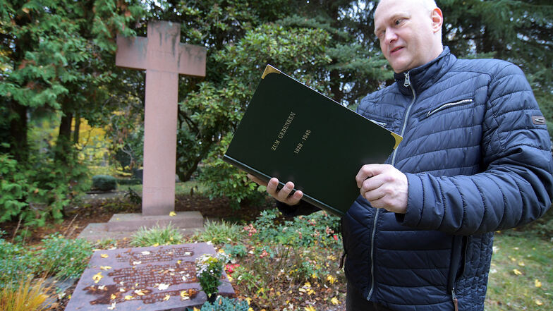 Vor der Gedenkplatte für die Opfer des II. Weltkrieges auf dem Harthaer Friedhof zeigt Kirchenvorstand Michael Fromm das neue Gedenkbuch, in dem die Namen und Daten der Opfer erfasst sind.