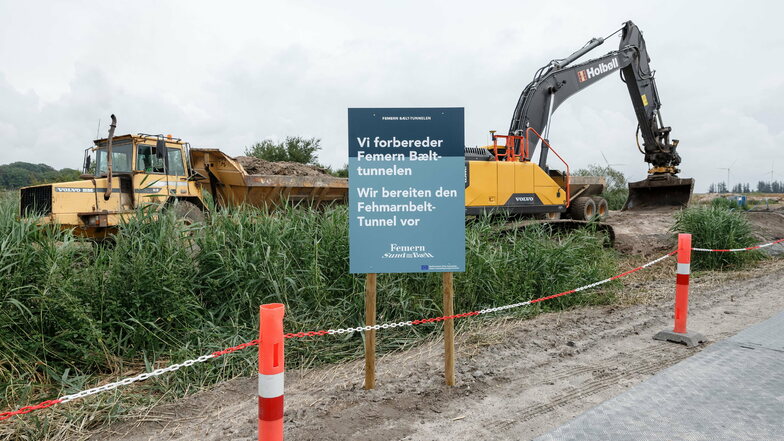Dänemark, Rødbyhavn: Baumaschinen heben hinter einem Schild mit der deutsch, dänischen Aufschrift "Wir bereiten den Fehmarnbelt-Tunnel vor" einen Entwässerungsgraben auf dem zukünftigen Baugelände aus.