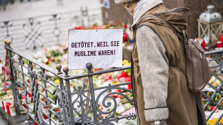 Eine Frau steht auf dem Marktplatz am Denkmal der Brüder Grimm. Blumen und Kerzen bedecken den Sockel des Denkmals.