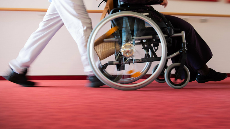 Ein Pfleger eines Pflegeheims schiebt eine Bewohnerin mit einem Rollstuhl. Im Landkreis Meißen spitzt sich die Lage in den Heimen wieder zu. In Coswig und Nossen kam zu erneuten Corona-Ausbrüchen.