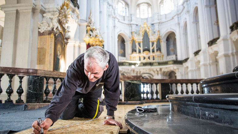 Handwerker Jens Strauch markiert eine Spanplatte, die auf dem Marmorfußboden der Hofkirche verlegt wird. Zum Auftakt der Sanierung werden der Fußboden und wertvolle Einbauten geschützt.