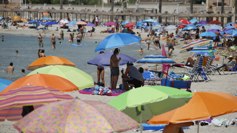 Urlauber suchen auf der Insel Mallorca am Strand Schatten unter Sonnenschirmen.