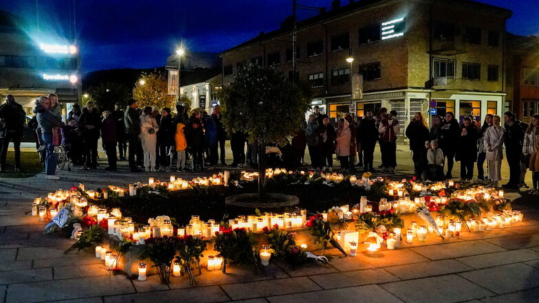 Personen stehen in Kongsberg vor Blumen und Kerzen, die in Gedenken an die Opfer niedergelegt wurden.