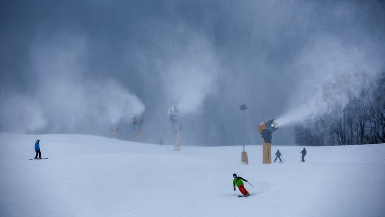 Wintersportler fahren bei laufenden Schneekanonen in der Skiarena Eibenstock.