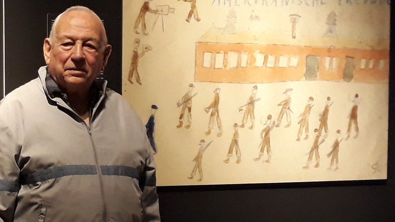 Thomas Geve steht neben einer vergrößerten Zeichnung während einer Ausstellung.