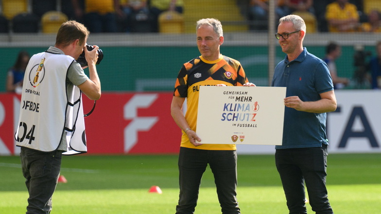 Dynamos Geschäftsführer Jürgen Wehlend und Alexander Wehrle - Vorstandsvorsitzender des VfB Stuttgart - halten eine Schild "Gemeinsam für mehr Klimaschutz im Fußball"· in den Händen.