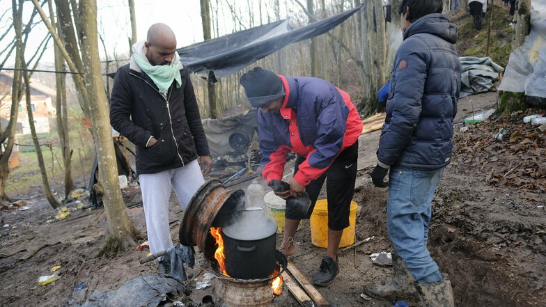 Migranten kochen auf einem aus Radfelgen gebauten Herd in einem provisorischen Lager