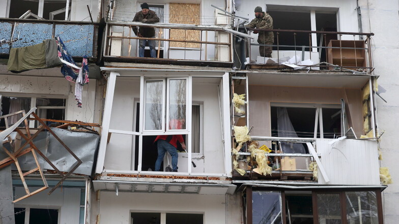 Männer stehen auf den beschädigten Balkonen eines durch einen Raketeneinschlag zerstörten Wohnhauses im ukrainischen Charkiw.