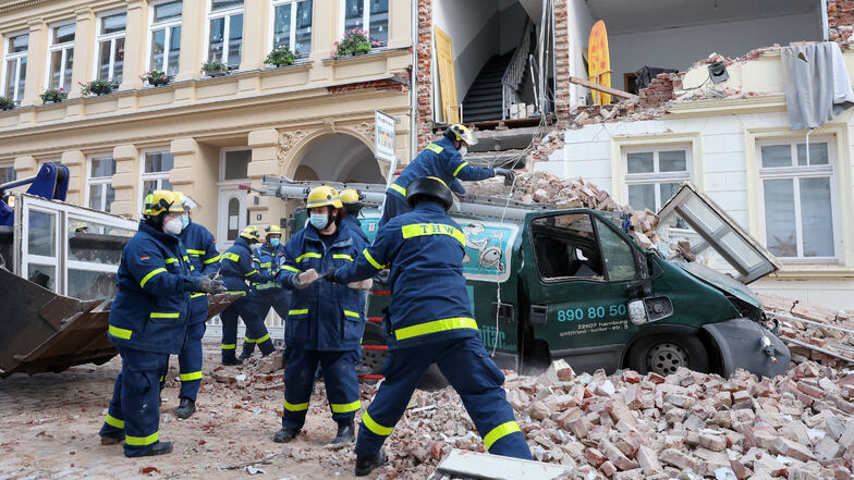 Einsatzkräfte vom Technischen Hilfswerk (THW) tragen Trümmerteile vor einem Haus in Hamburg ab, dessen Fassade eingestürzt ist.