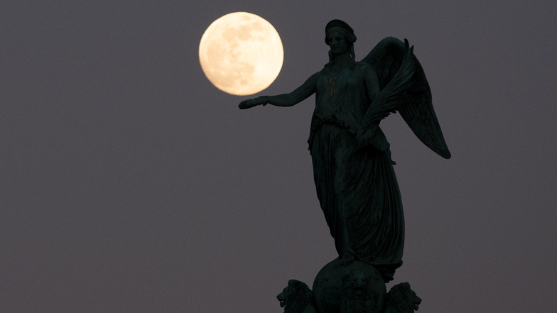 Der fast volle Mond steht am Abendhimmel hinter der Concordia Säule auf dem Schlossplatz in Stuttgart.