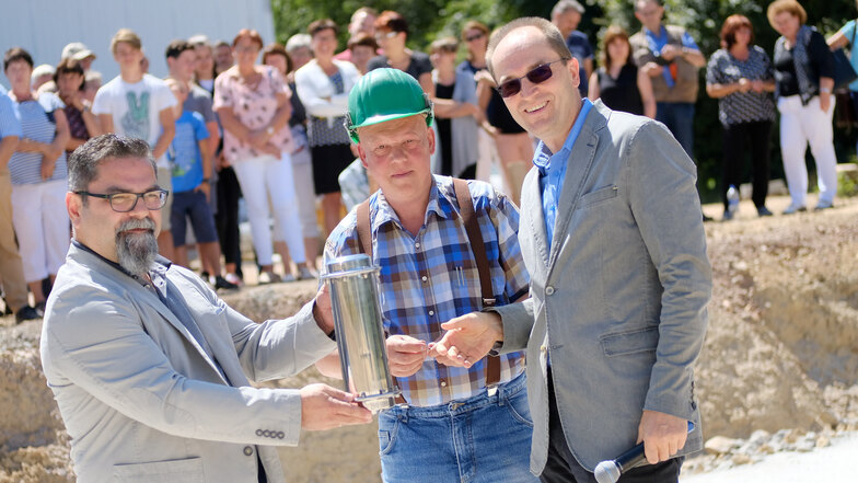 Bürgermeister Uwe Anke (rechts) und Schulleiter Michael Janik (links) nehmen mithilfe von Steffen Helm, Mitarbeiter der Baufirma, die Grundsteinlegung für die neue Sporthalle in Nossen vor.