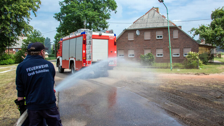 Feuerwehrleute verteilen Wasser im evakuierten Ort und versuchen damit die Wege feucht zu halten.