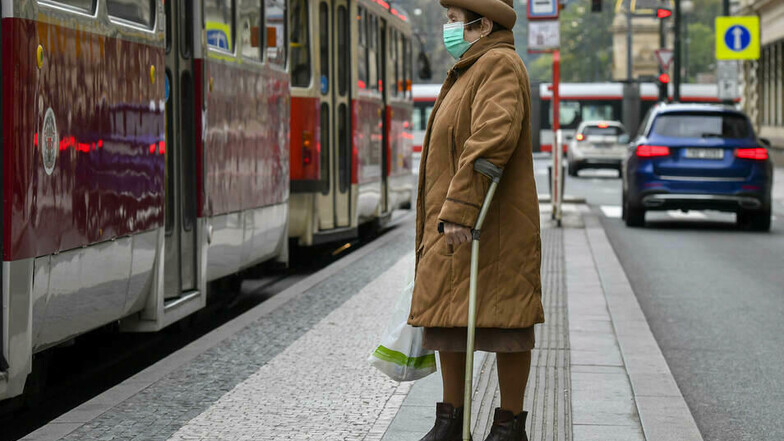 Eine Frau mit Mund-Nasen-Schutz wartet in Prag auf die Straßenbahn.
