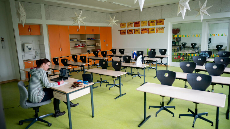 Eine Lehrerin sitzt in ihrem leeren Klassenzimmer vor einem Laptop.