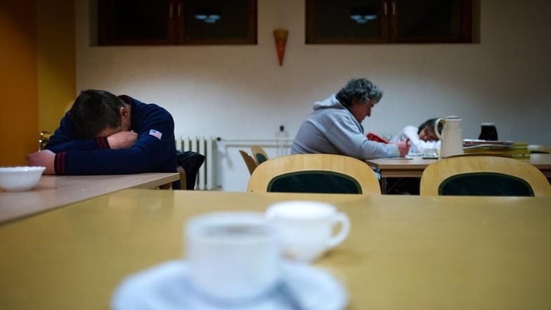 Ein Besucher des Nachtcafés der St. Petrus Gemeinde in Dresden-Strehlen liegt im Aufenthaltsraum mit dem Kopf auf dem Tisch (l) und ruht sich aus.