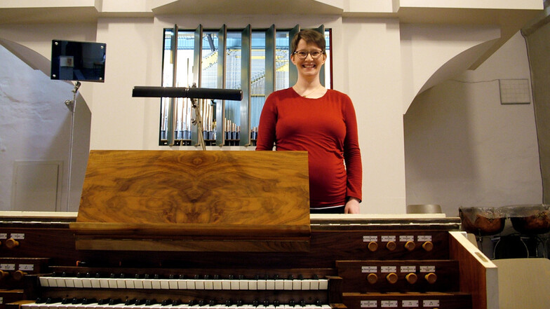 Claudia Hofmann, die derzeit ihr erstes Kind erwartet, hinter ihrem Arbeitsplatz und vor ihrem Arbeitsgerät – zwischen dem Spieltisch und der Orgel der katholischen Wittichenauer Pfarrkirche St. Mariä Himmelfahrt.