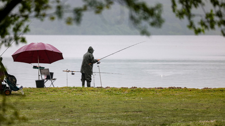 Ein Angler steht bei Regen an einem See.