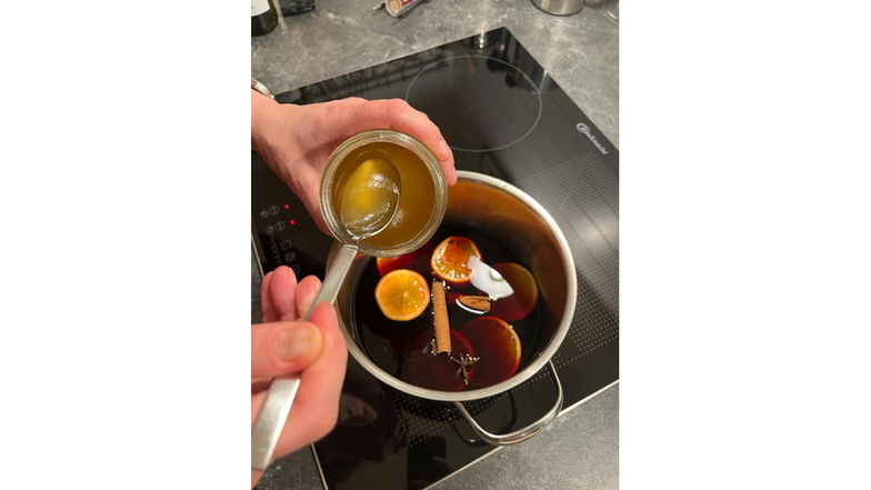 Gewürze, Orangenscheiben und Honig werden in den warmen Wein untergerührt.